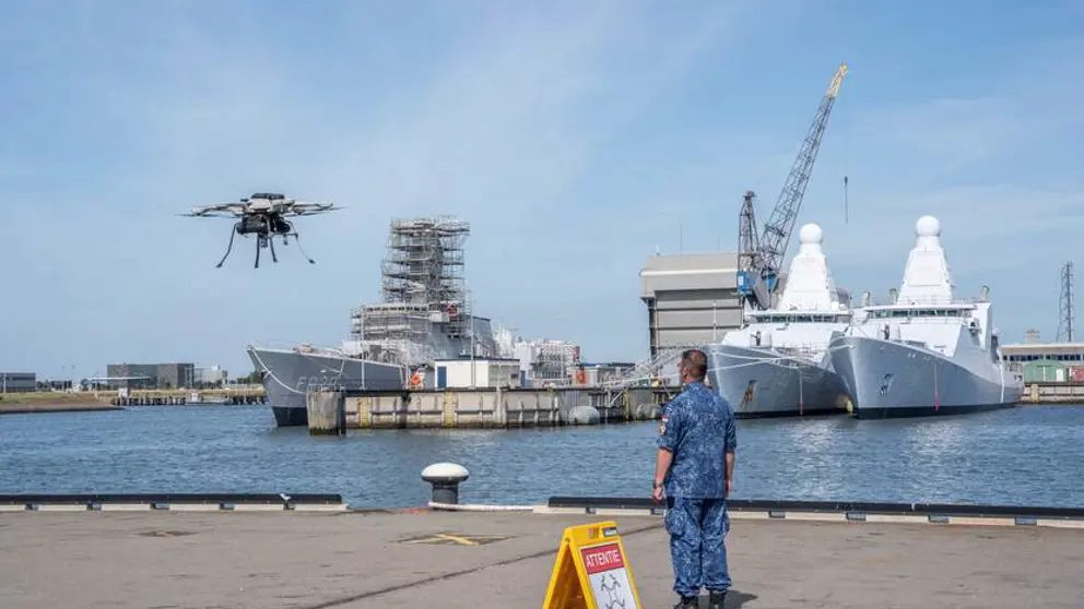 Militair staat op kade en kijkt naar drone die opstijgt.