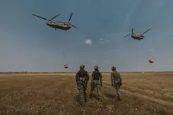 Militairen op de rug gezien. In de lucht 2 helikopters met waterzakken.