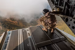 Een militair kijkt vanuit de laadruimte van een helikopter naar beneden.