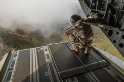 Een militair kijkt vanuit de laadruimte van een helikopter naar beneden.