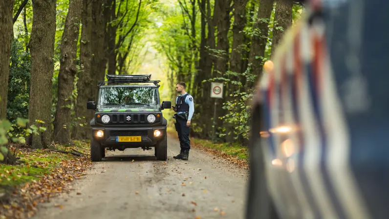 Wachtmeester Joris spreekt met een bestuurder in een bosgebied op de Veluwe.
