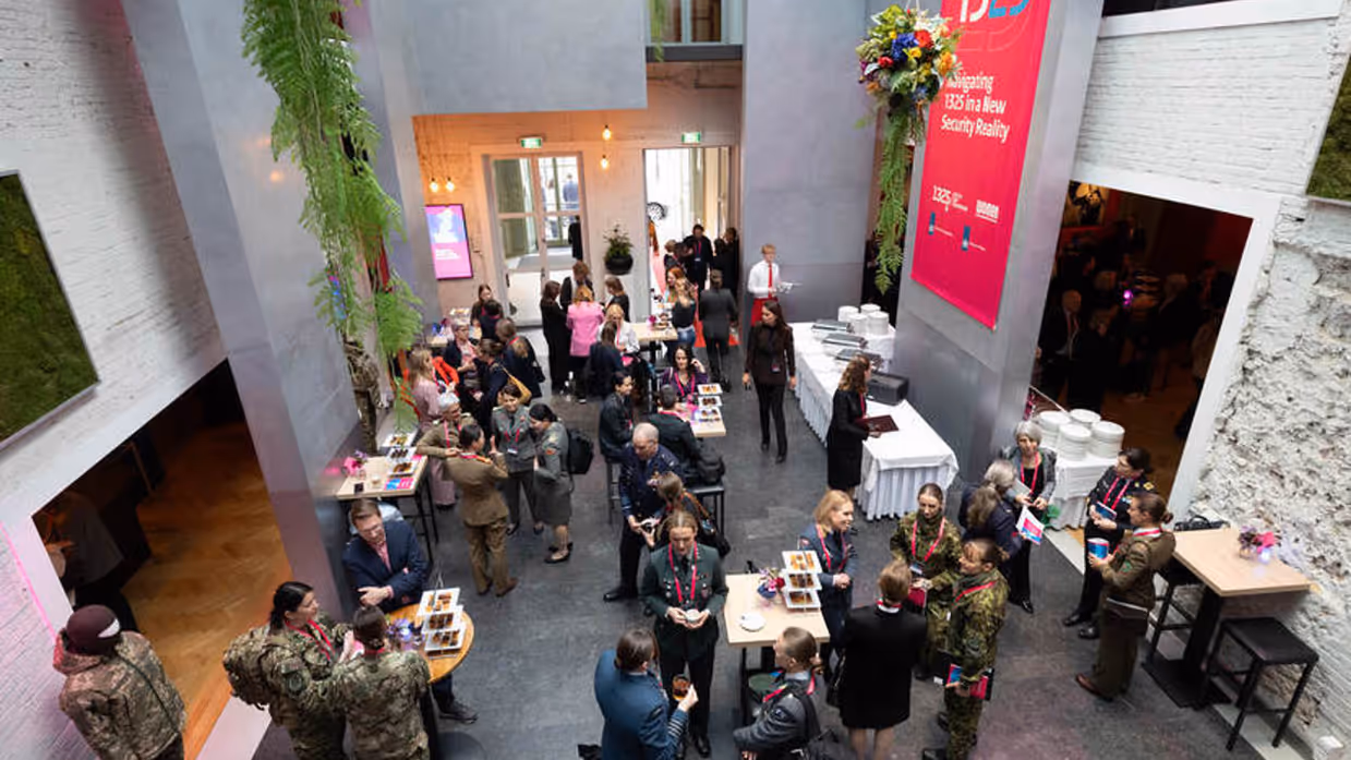 Deelnemers van bovenaf gezien. Ze staan aan tafeltjes met koffie en thee.