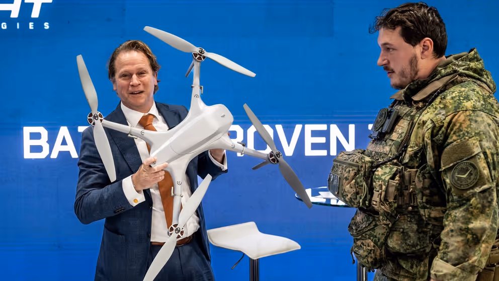 Staatssecretaris Gijs Tuinman op de beursvloer met een drone in zijn hand. Een militair naast hem in uniform. 