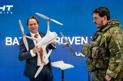 Staatssecretaris Gijs Tuinman op de beursvloer met een drone in zijn hand. Een militair naast hem in uniform. 