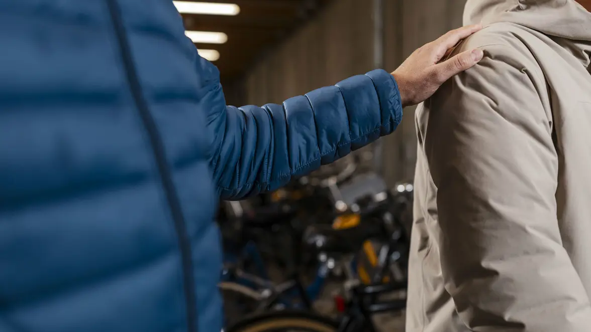 Close-up van een persoon die een hand op de schouder van een potentiele informant legt in een ruimte vol geparkeerde fietsen.