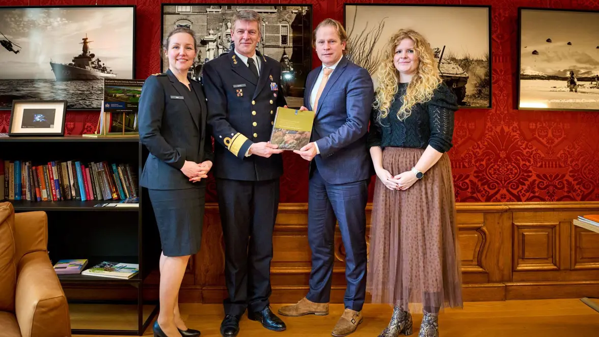 Vier mensen poseren bij de overdracht van een rapport.