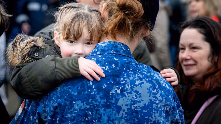 Een jong meisje kijkt over de schouder van een vrouw van wie de rug en een staartje zichtbaar zijn.