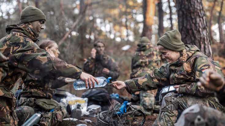 De deelnemers lunchen. Eentje schenkt water in met een plastic fles.