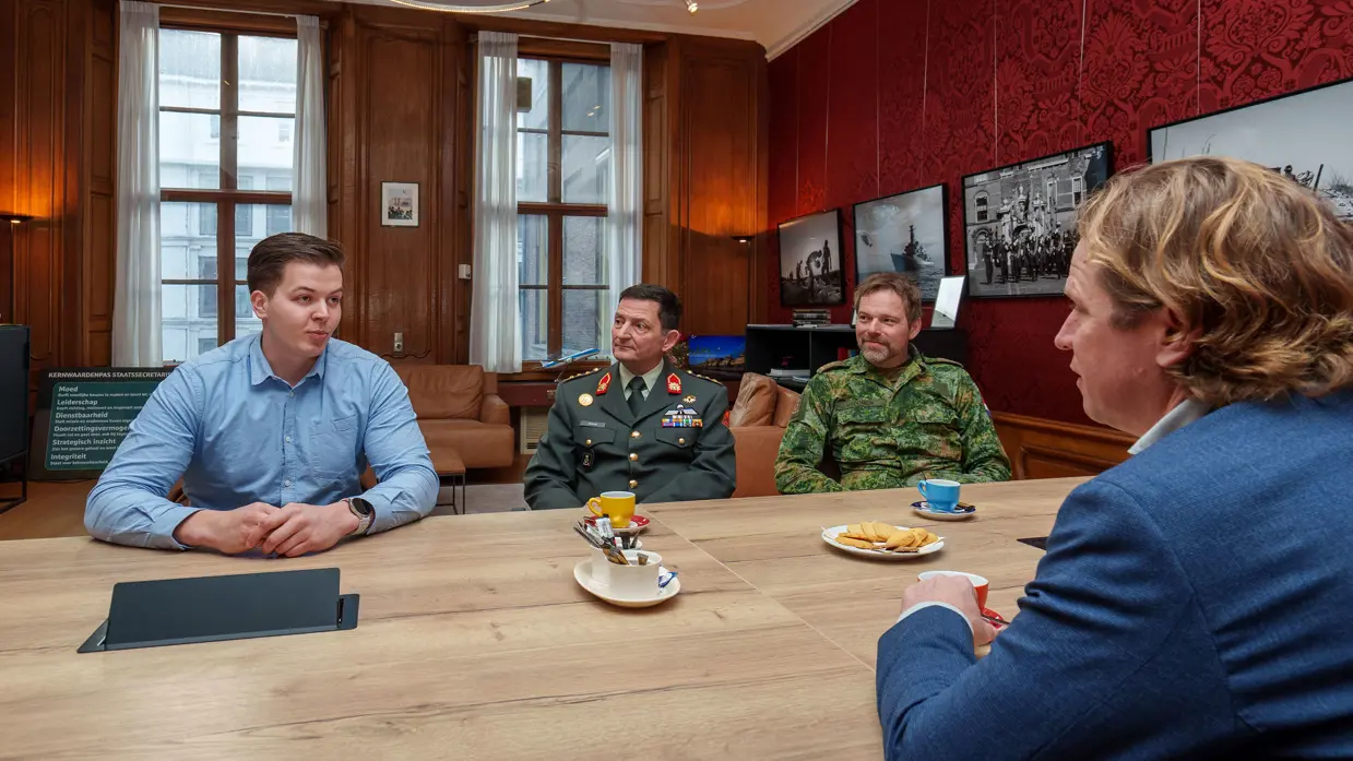 Defensiemedewerker zit aan tafel met 2 hoge militairen en de staatssecretaris.