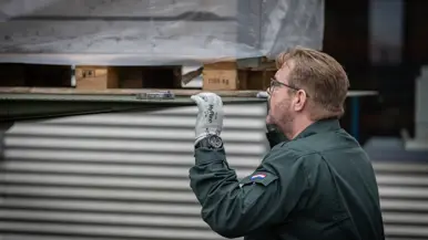 Een medewerker monitort van dichtbij hoe een pallet wordt uitgeladen. Op de tweede foto een medewerker, gezeten achter zijn bureau.