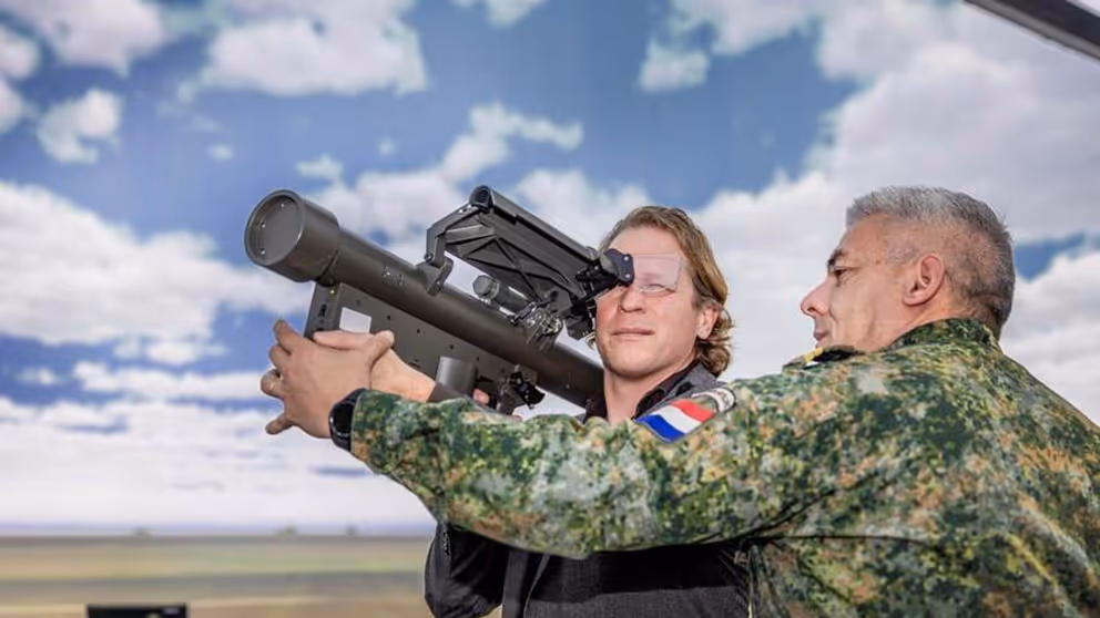 Staatssecretaris Tuinman kijkt door een vernieuwde Stinger-simulator. Aan de rechterkant een militair die de simulator vasthoudt.