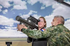 Staatssecretaris Tuinman kijkt door een vernieuwde Stinger-simulator. Aan de rechterkant een militair die de simulator vasthoudt.