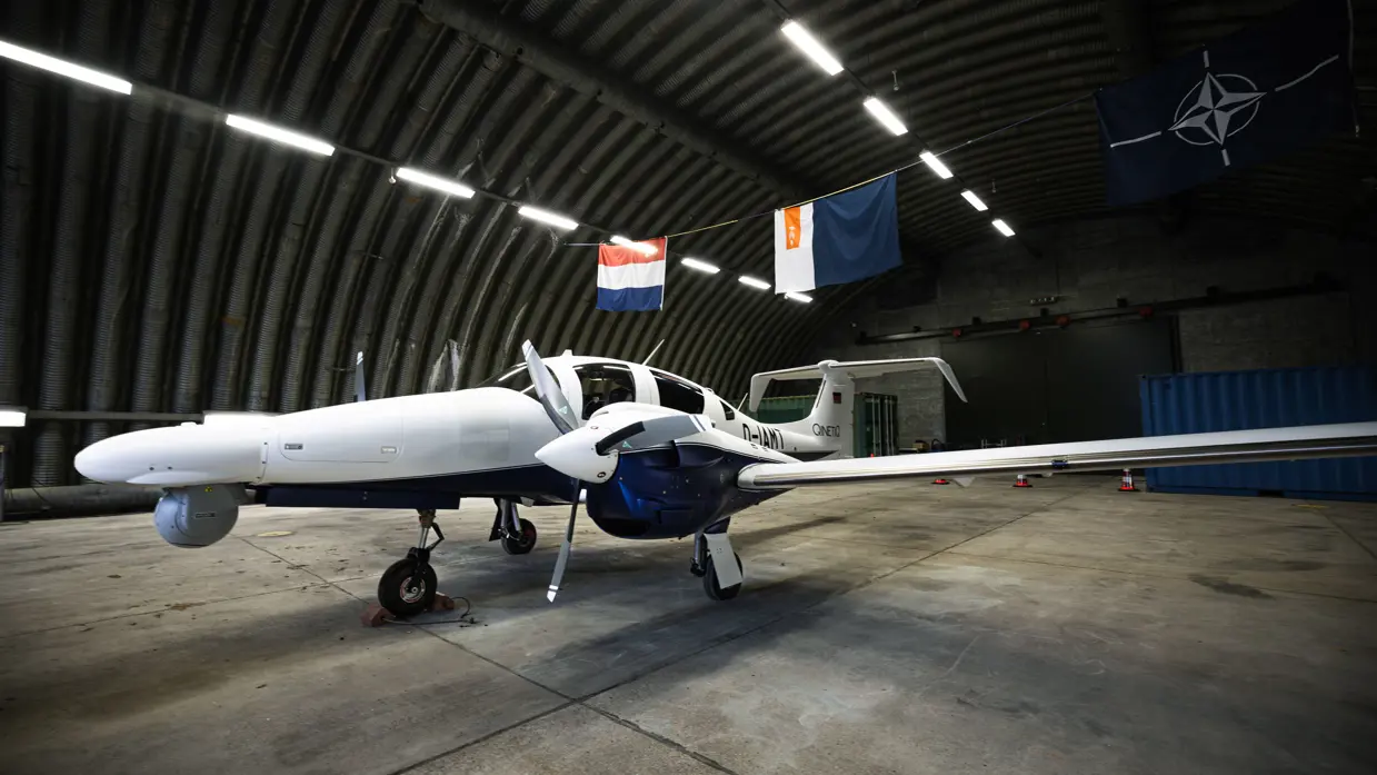 Nieuwe vliegtuig van de Marechaussee in een hangar met de Nederlandse vlag en vlag met logo van de KMar er boven.