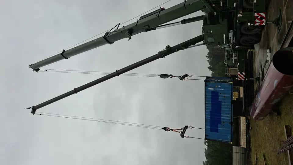 Twee hijskranen naast elkaar hijsen materialen op. 
