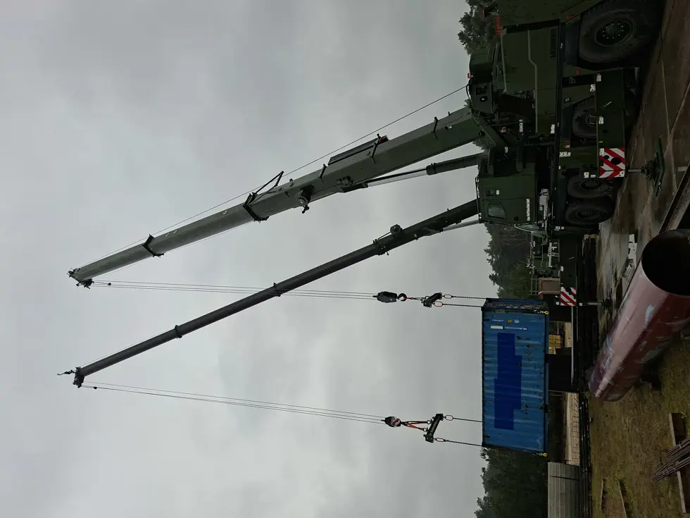 Twee hijskranen naast elkaar hijsen materialen op. 