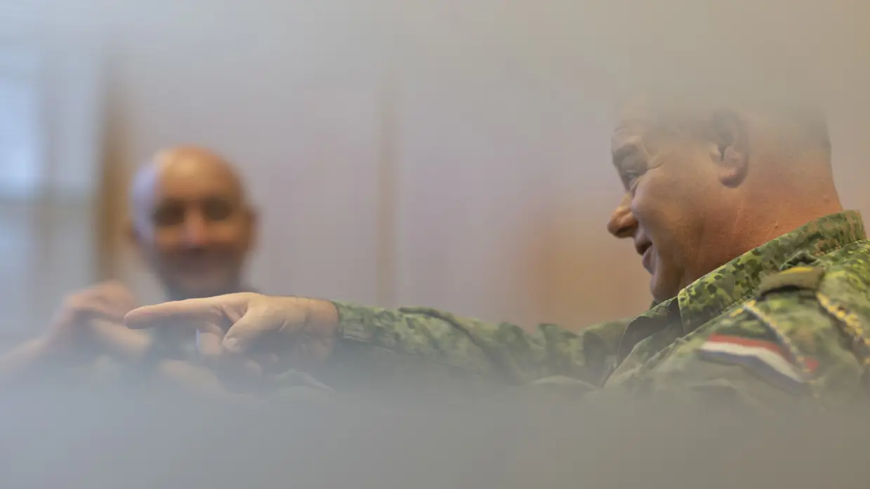 Oud-Luchtmachtadjudant Terry Venhovens spreekt geanimeerd en wijst met zijn wijsvinger. De nieuwe Luchtmachtadjudant Johan de Rooij kijkt Venhovens op de achtergrond aan.    