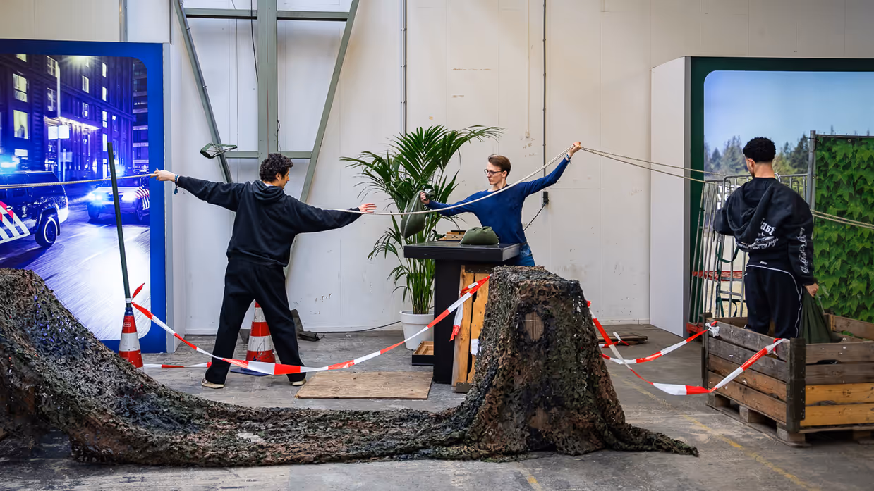 Diverse beelden van de fysieke uitdagingen, van links naar rechts: een team loopt met de handen aan een touw, waarbij ze over hindernissen moeten komen. Een team is gemaskerd en moet een ei in een dop over een parcours leiden. Rechts hangen twee deelnemers aan een rekstok.