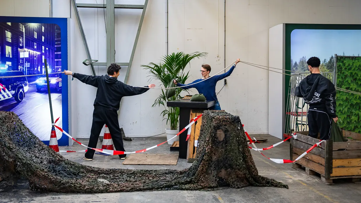 Diverse beelden van de fysieke uitdagingen, van links naar rechts: een team loopt met de handen aan een touw, waarbij ze over hindernissen moeten komen. Een team is gemaskerd en moet een ei in een dop over een parcours leiden. Rechts hangen twee deelnemers aan een rekstok.