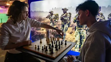 Van links naar rechts: een jongeman pakt iets van een veldbedje met een slaapzaak in een grote zaal. Een militair in een blauw uniform legt iets uit aan een groepje toehoorders in een donkere zaal. Twee man zitten aan een schaakbord met een poster van Defensie op de achtergrond. Een man in uniform met strepen op de schouder in bespreking met vijf anderen.