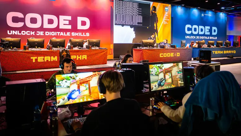 Vier mensen zitten met koptelefoon achter een computer, ze spelen games.