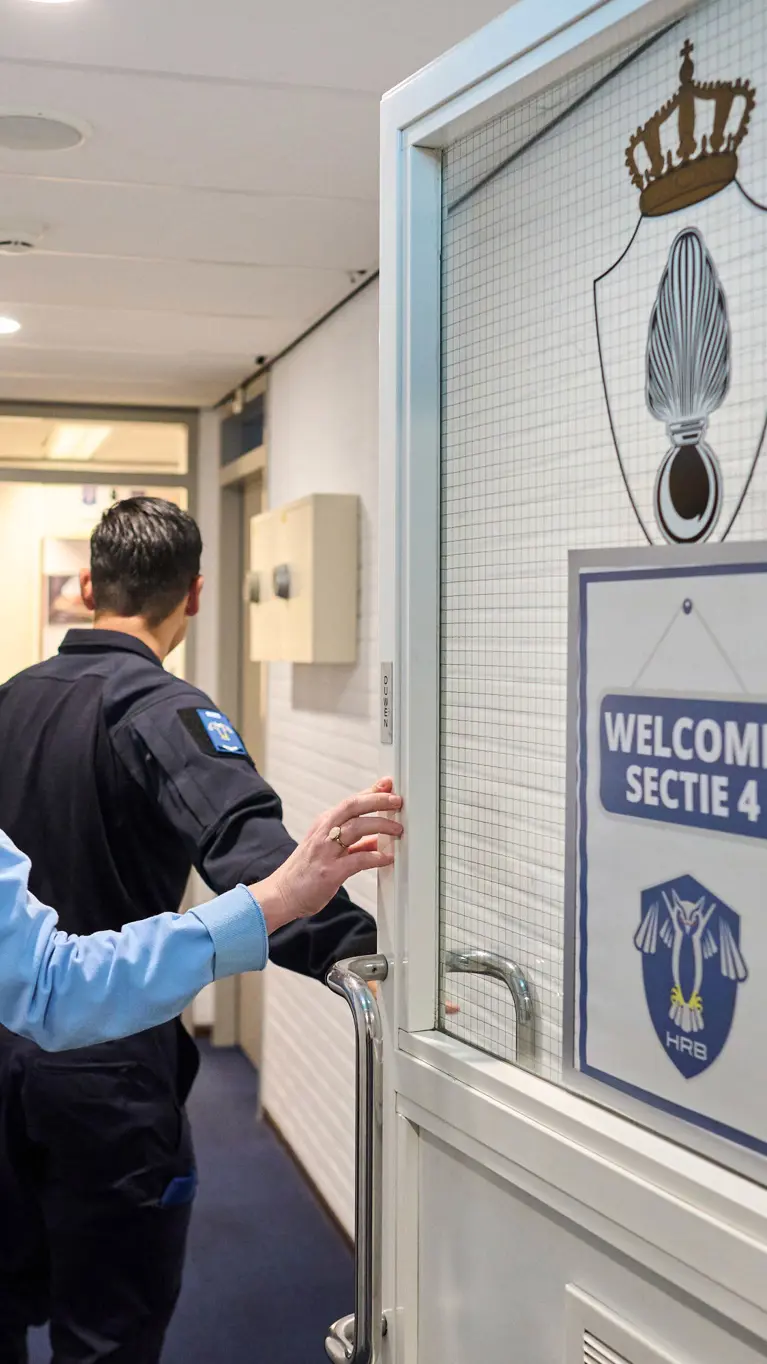 Adjudant Carolien en kapitein Tobias stappen door een deur waarop ‘Welcome Sectie 4’ wordt afgebeeld.