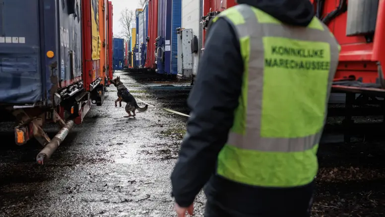 Een aangelijnde diensthond van de KMar snuffelt aan een van de vele trailers.