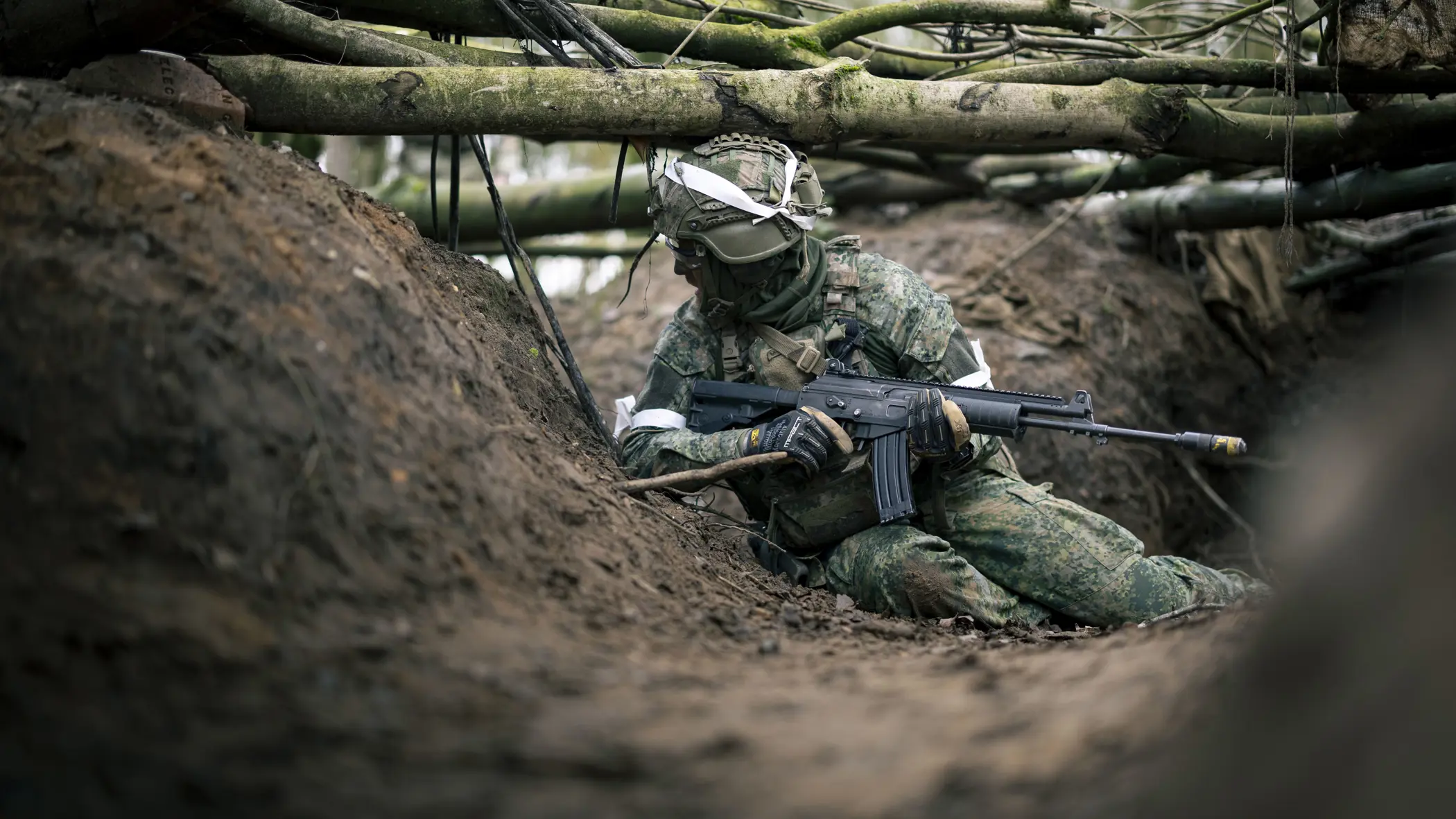 Een militair zit op zijn heupen in een loopgraaf. 