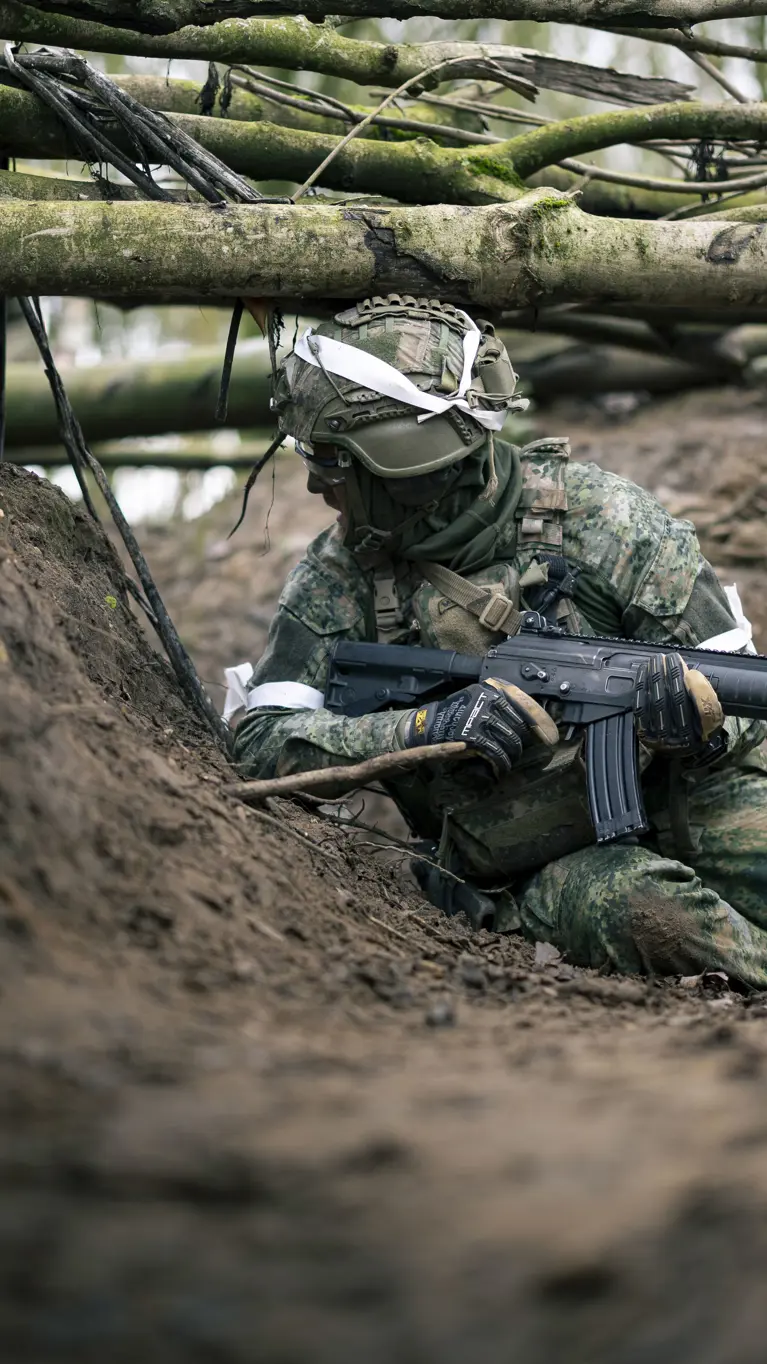 Een militair zit op zijn heupen in een loopgraaf. 