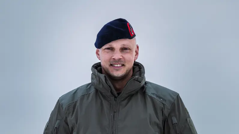 Portret van kapitein der mariniers Marnix, vlieger bij het maritieme helikoptersquadron, in winterkleding en baret staand in een besneeuwd landschap.