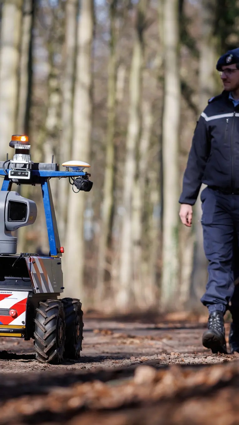 Een marechaussee loopt samen met de Roboguard door het bos.