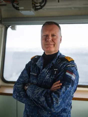 Commandeur Pastoor in maritiem camouflage-uniform aan boord van een marineschip. 
