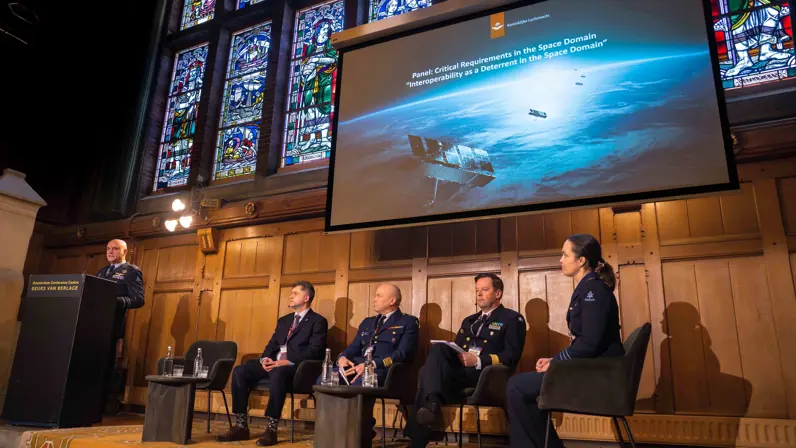  Vijf deelnemers aan een paneldiscussie op een podium. Generaal Steur staat achter een katheder en houdt een speech.