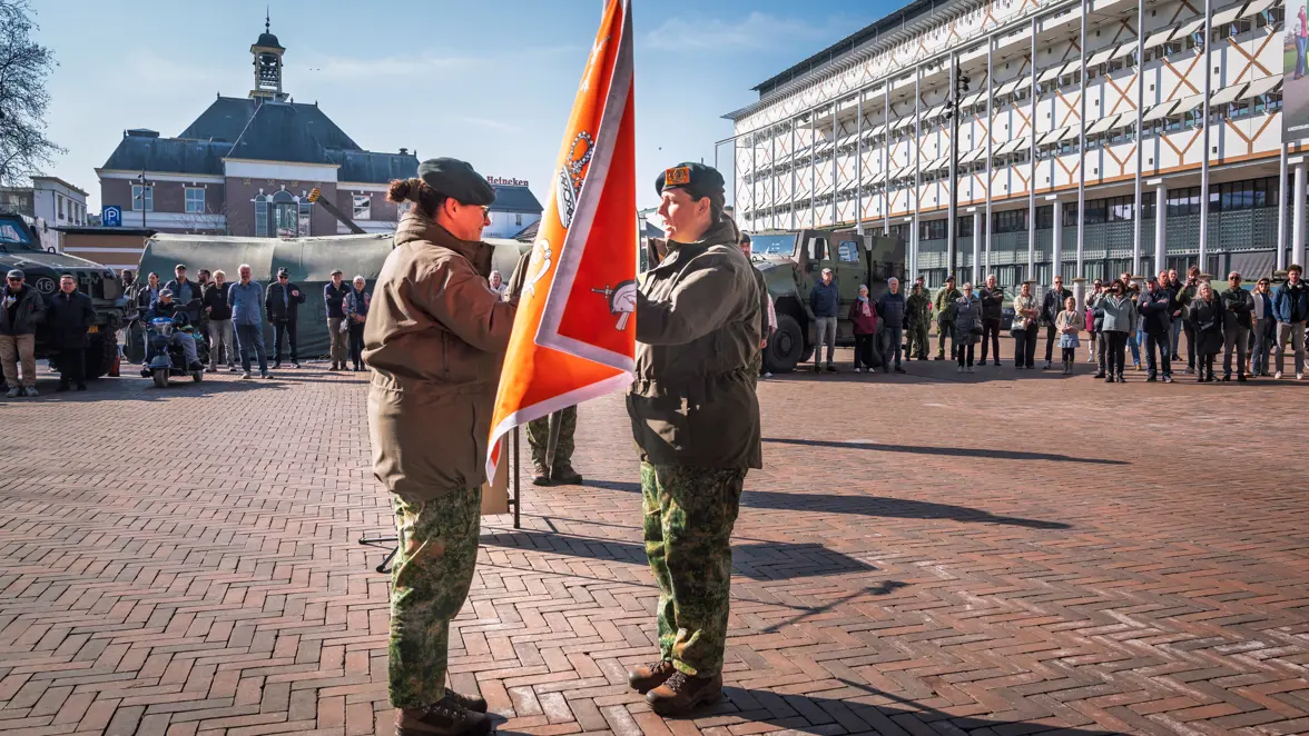 Twee militairen houden vlag vast tijdens ceremonie op plein. 