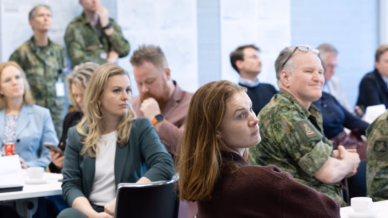 Zittende mensen die allemaal dezelfde kant op kijken. 3 mensen dragen gevechtskleding.