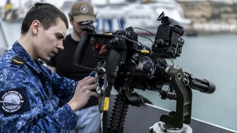 Marinepersoneel monteert een minigun op een reling. 