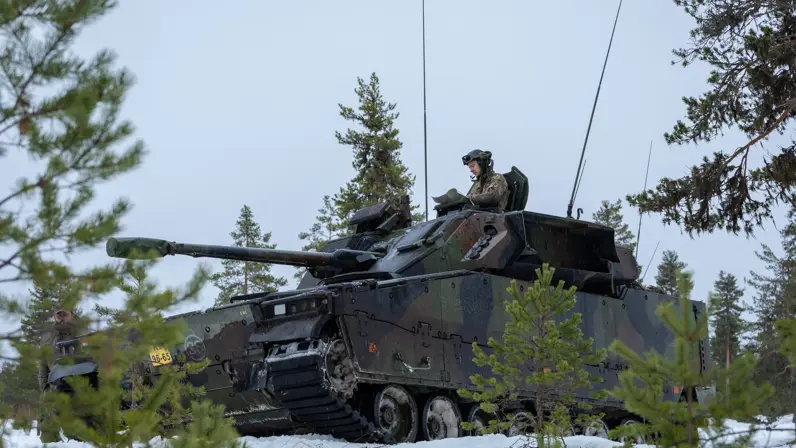 Een militair voertuig rijdt door een winters landschap.