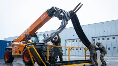 Links: een versleten rubberen band track, rechts: met een heftruck wordt een rubberen band track omhoog gehesen.