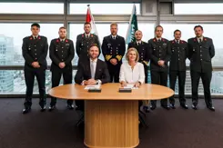 2 mensen zitten aan tafel, achter ze staan reservisten.