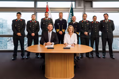 2 mensen zitten aan tafel, achter ze staan reservisten.