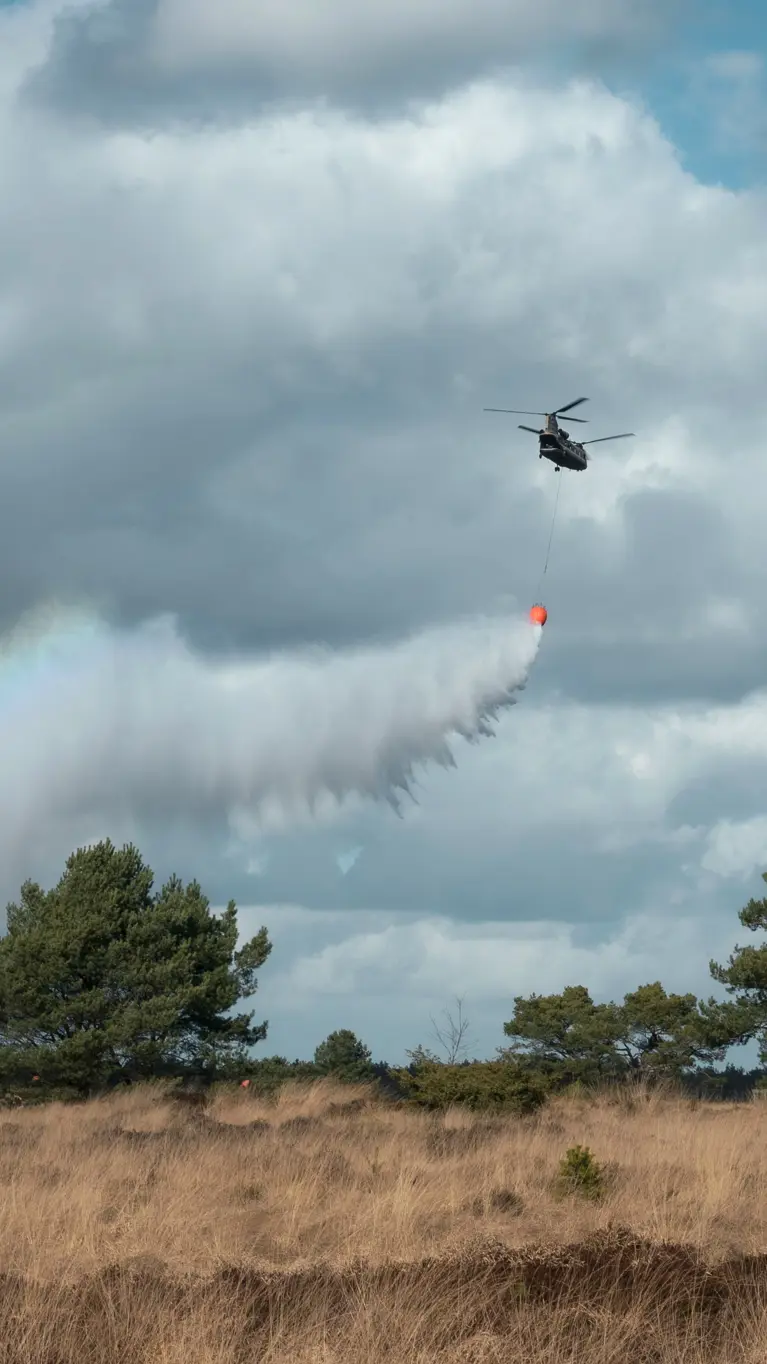 Een helikopter dropt water boven de hei. In de waternevel ontstaat een regenboog.