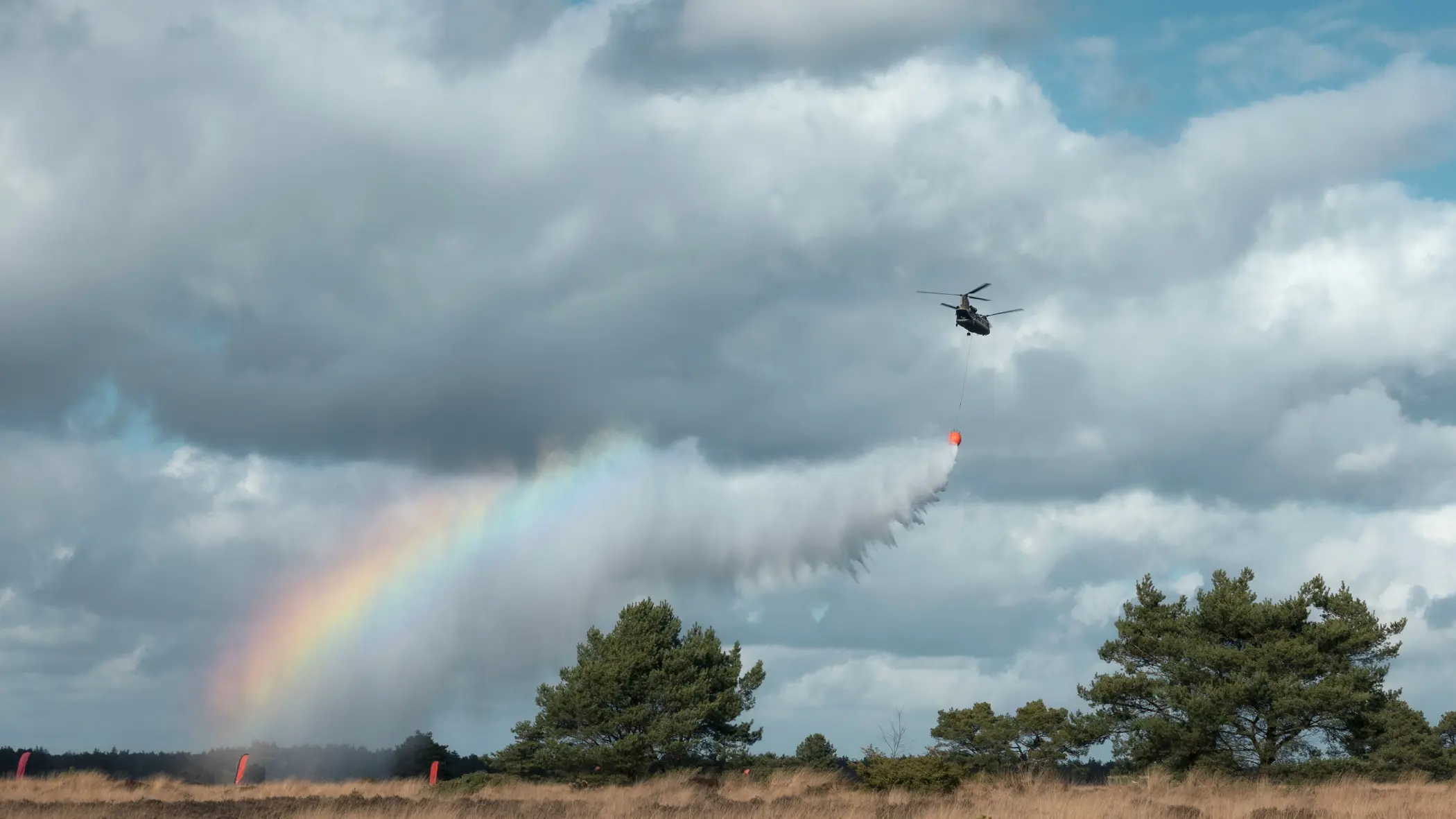 Een helikopter dropt water boven de hei. In de waternevel ontstaat een regenboog.