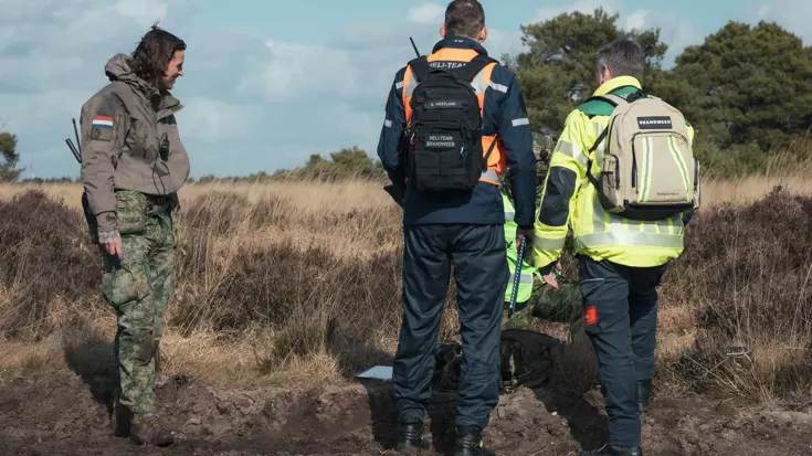Een militair en twee brandweermannen overleggen op de hei.