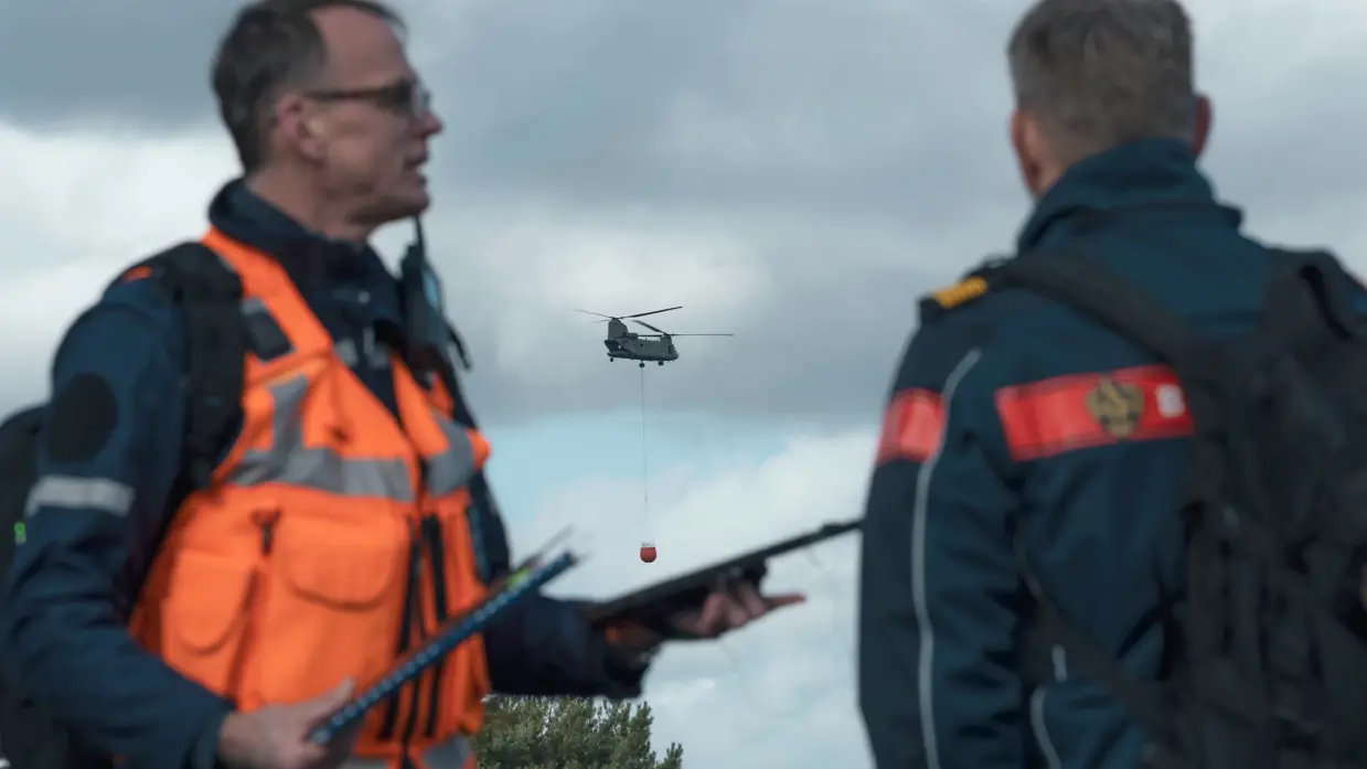Twee personen overleggen op een militair oefenterrein.