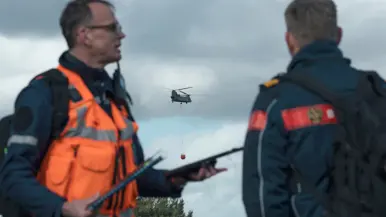 Twee personen overleggen op een militair oefenterrein.
