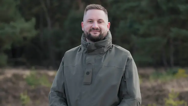 Een militair poseert met handen over elkaar op de hei.