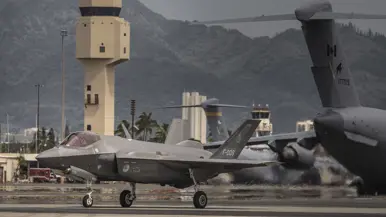 Een F-35 taxiet op Hawaii voor de verkeerstoren langs. In de achtergrond staan C-17 transportvliegtuigen van de VS en uit Canada