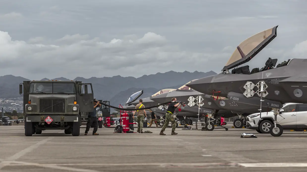 Luchtmachtpersoneel sjouwt brandstofslangen uit een Amerikaanse tankwagen naar een F-35. In de achtergrond zijn bergen te zien.