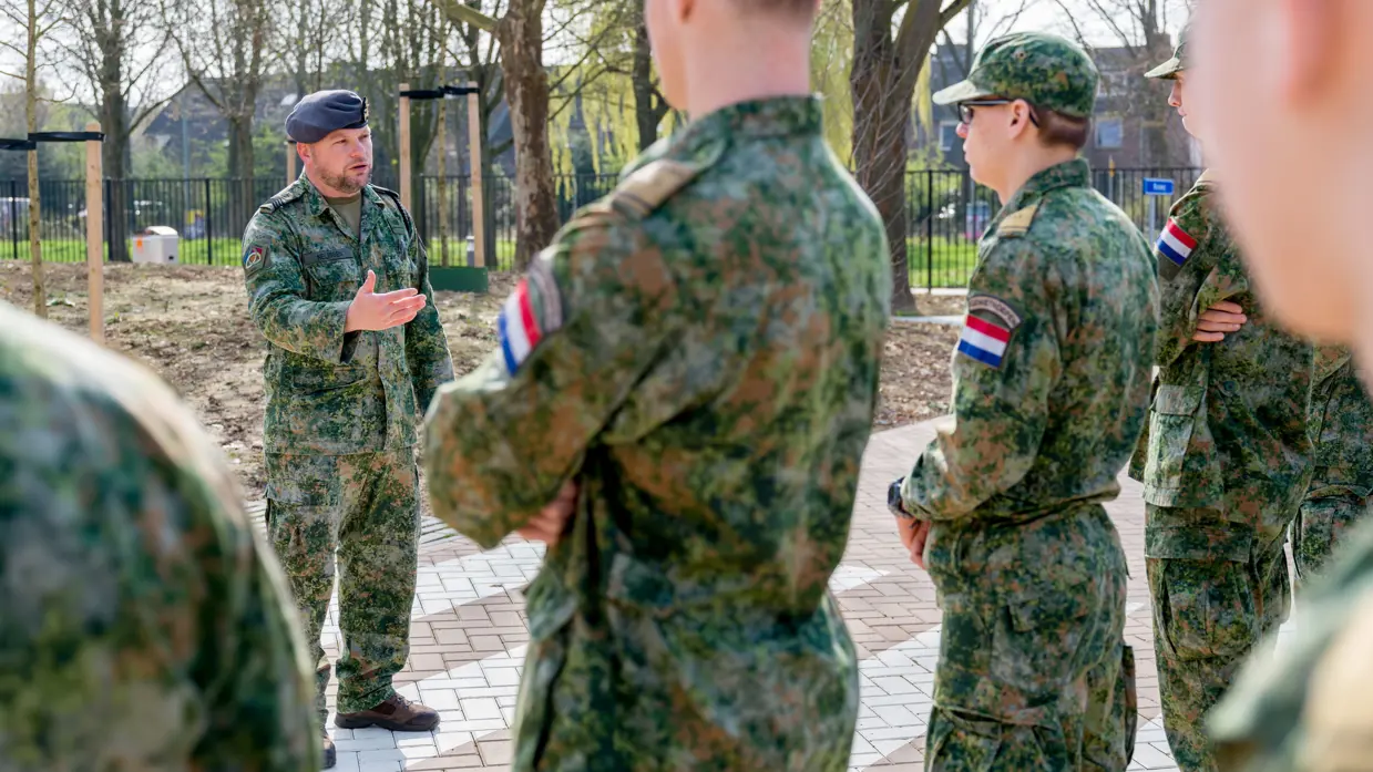 Buiten staat een rijtje jongeren in gevechtspak. Ervoor staat sergeant-majoor Tim Nelissen die hen toespreekt.