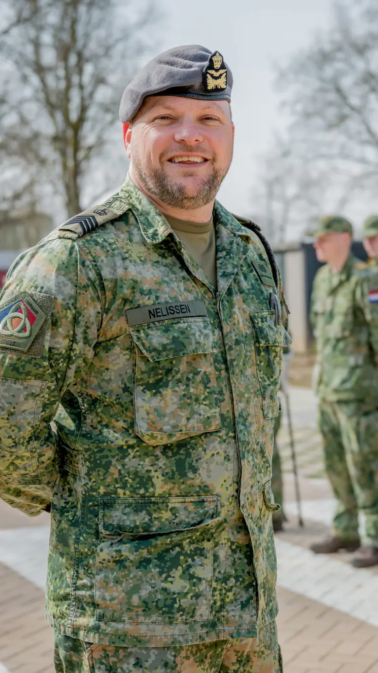 Sergeant-majoor Tim Nelissen poseert buiten voor twee rijen opgestelde militairen met militaire petjes op.
