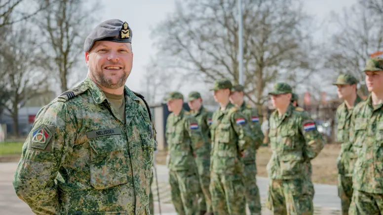 Sergeant-majoor Tim Nelissen poseert buiten voor twee rijen opgestelde militairen met militaire petjes op.